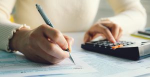 Close-up of someone filing taxes; using a calculator with one hand and writing with the other