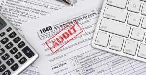 An IRS tax form, stamped "AUDIT", amongst other documents, a calculator, and a white keyboard