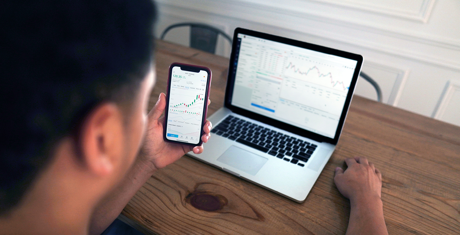 A man views a stock performance on both a cell phone and a laptop