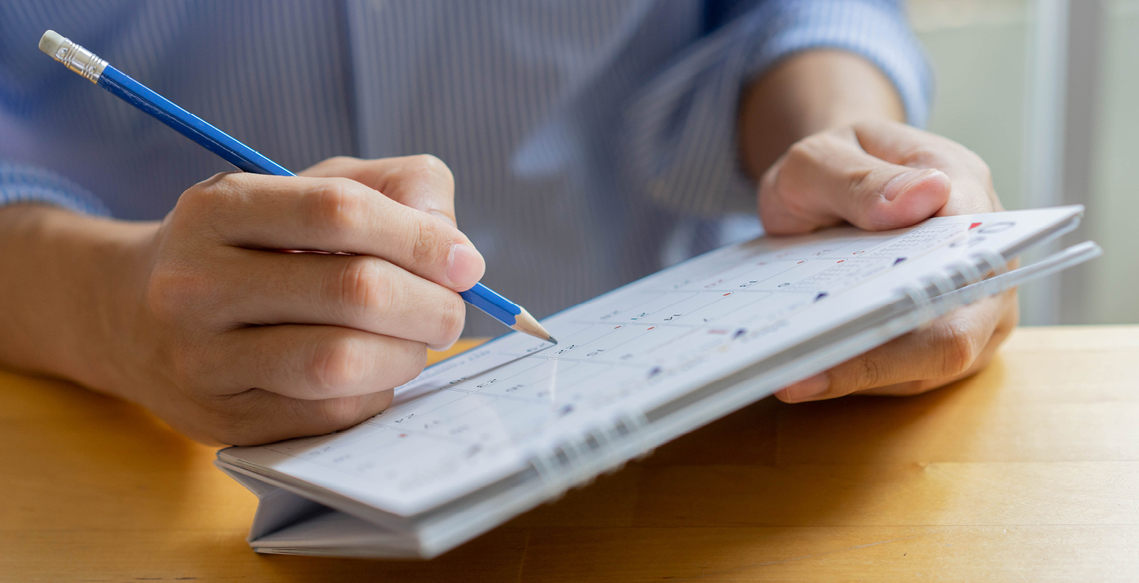 A man holds a desktop calendar in his hands, and is writing on it with a blue pencil