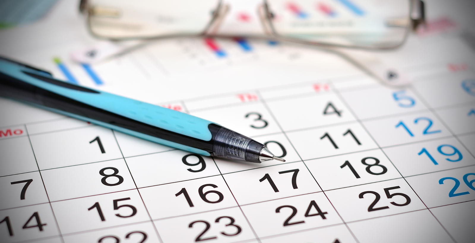 An up-close image of a blue and black pen and a pair of reading glasses on top of a calendar page