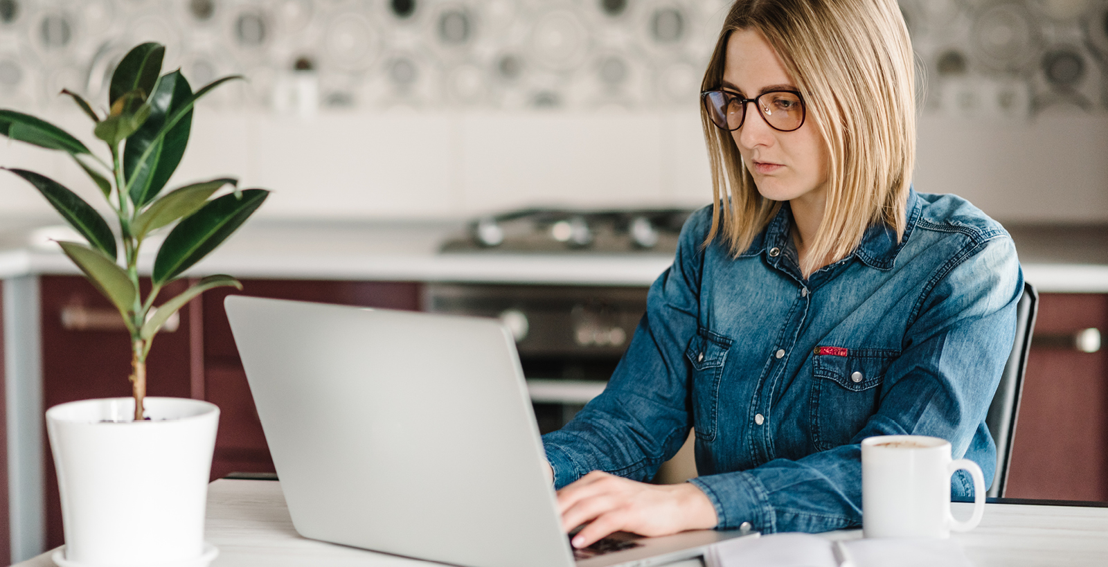 Young woman sits at table looking intently at her laptop screen