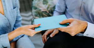 An close-up image of an older person and a younger person handing off a blue envelope.