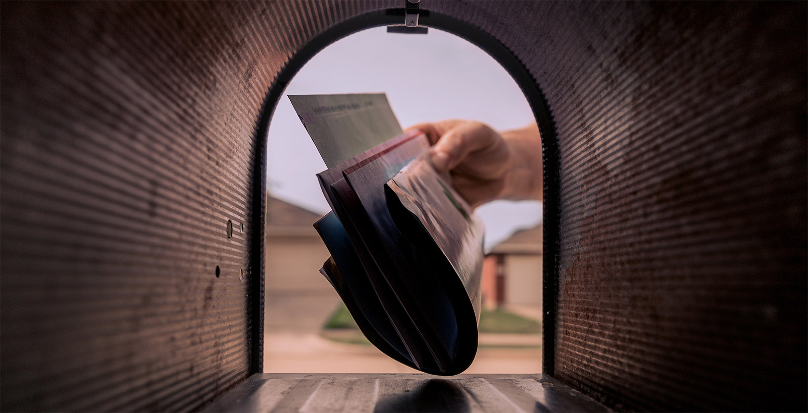 From inside a metal mailbox, a hand is seen pulling out a stack of mail.