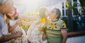 A little girl kisses her grandmother on the cheek. Her sister sits on their grandfathers' lap, smiling at one another.