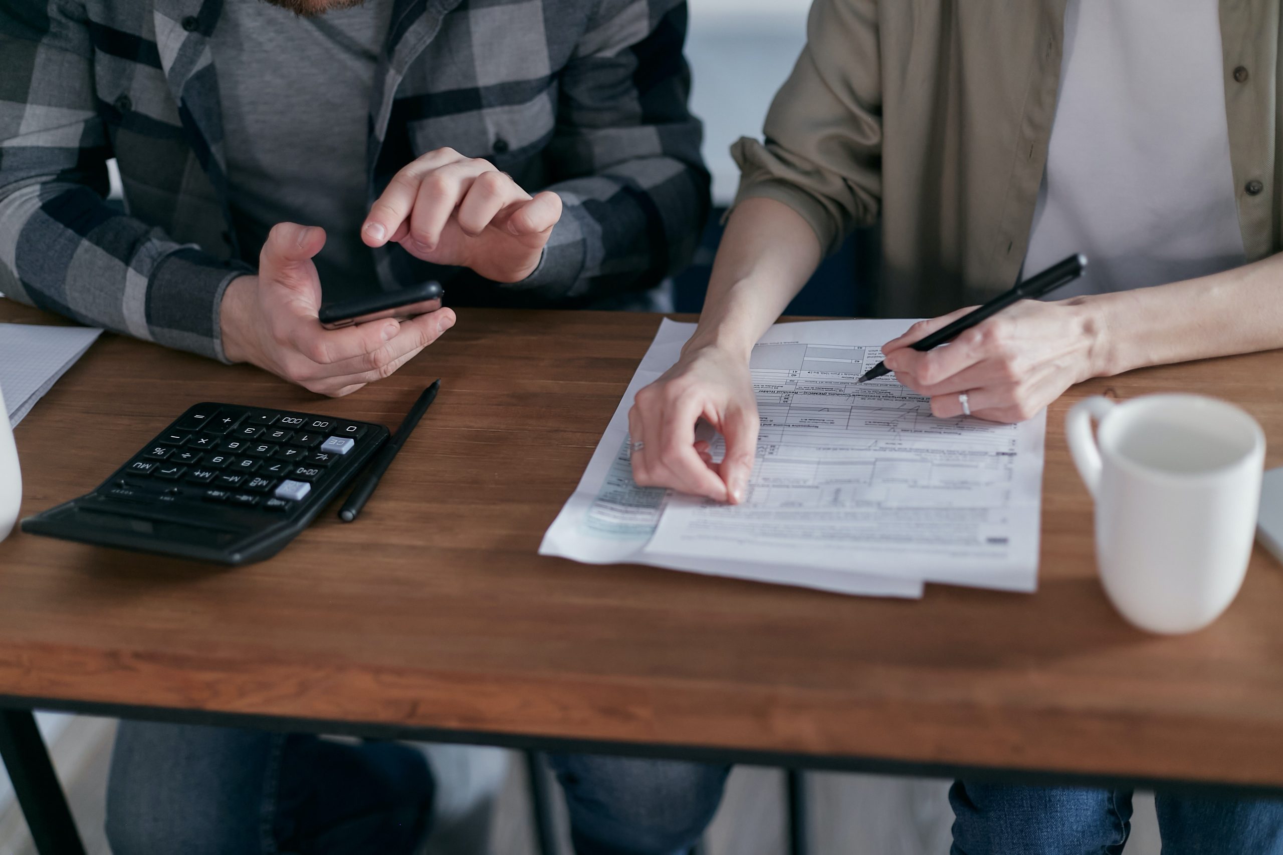 two people reviewing tax forms at desk with calculator and cup of coffee