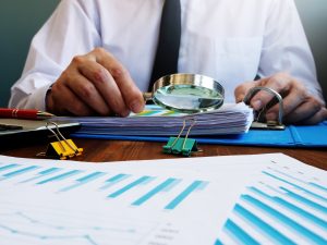 Auditor makes internal audit of company and checks financial report with magnifying glass.