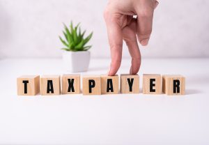 the word taxpayer wooden cubes with burnt letters, debts, gray background top view.