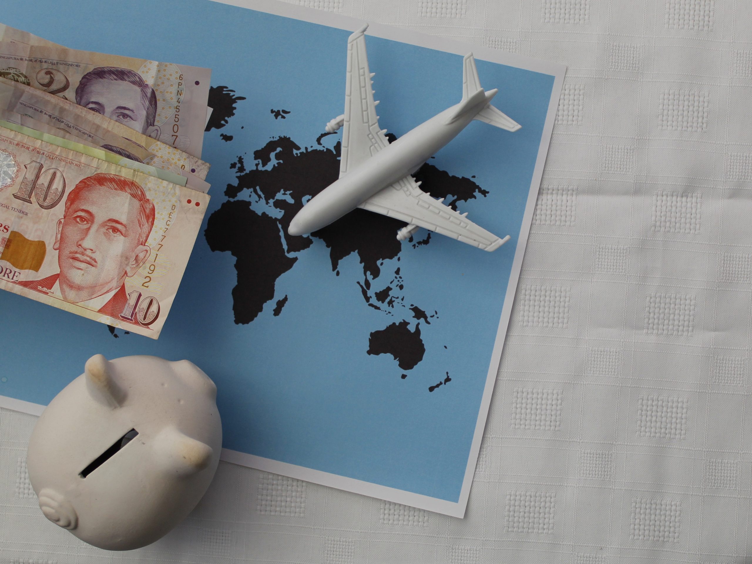 Singaporean money, figure of an airplane and piggy bank on a sheet with a world map